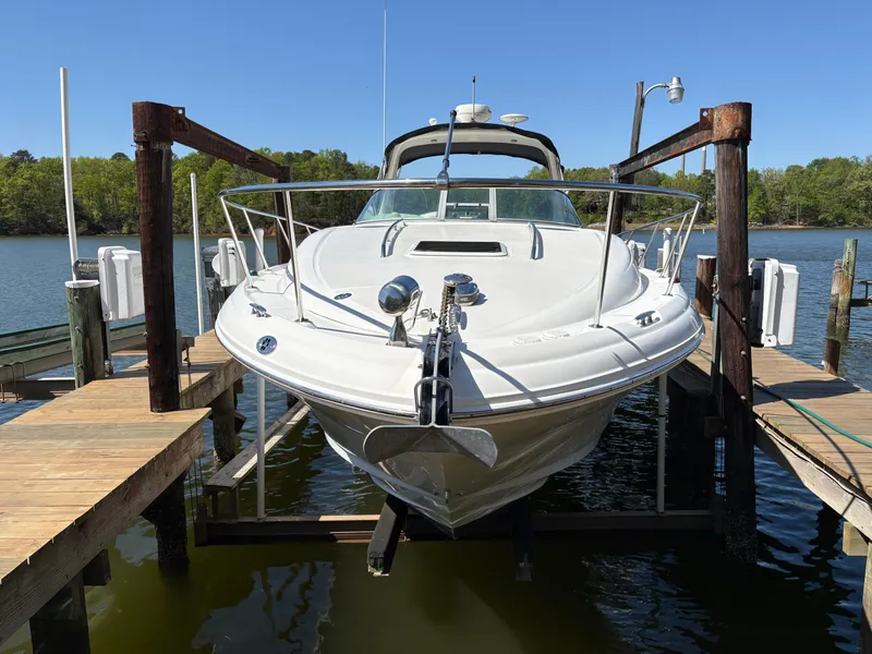 The Image of A 2006 Sea Ray Sundancer 320 is on a boat lift at a calm lakeside. - 0