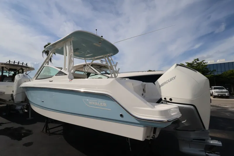 Slide: The Image of A 2027 Boston Whaler 240 Vantage with a blue hull and white top, parked next to another boat. - 3