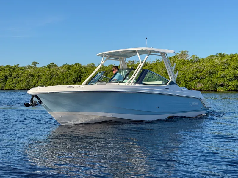 Slide: The Image of A 2027 Boston Whaler 240 Vantage cruising on calm water with green shoreline in the background. - 3