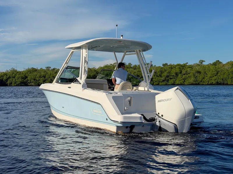 Slide: The Image of A 2027 Boston Whaler 240 Vantage cruising on calm waters with lush greenery in the background. - 5