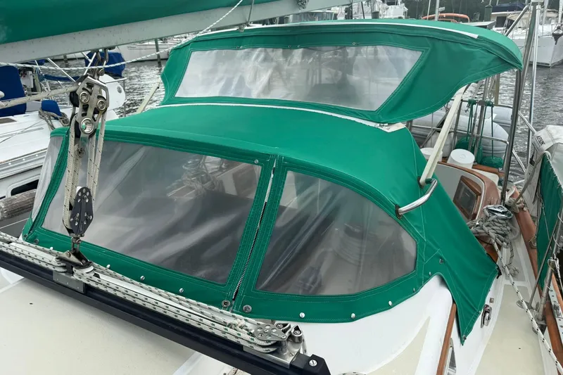 Slide: The Image of 1989 Cabo Rico 34 sailboat with green canvas cover and clear windows at a marina. - 12