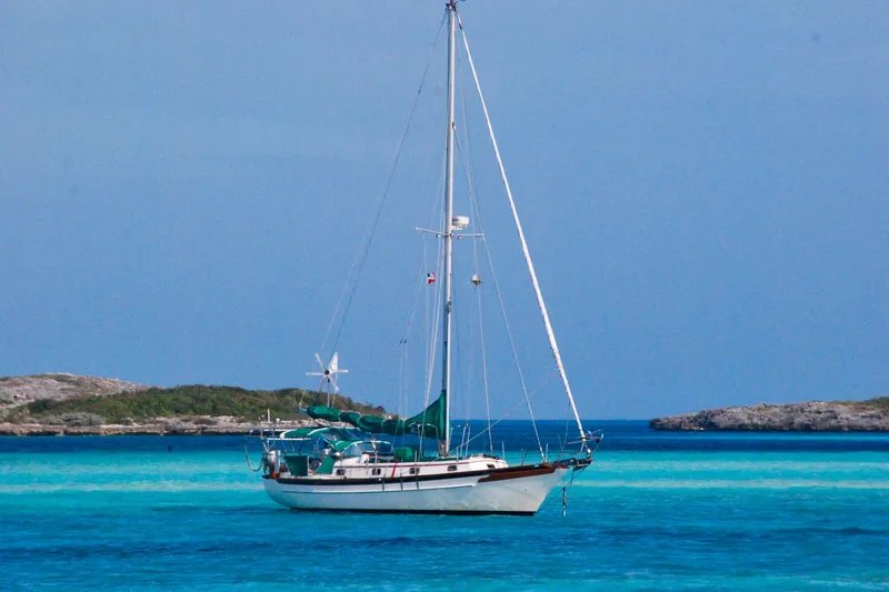 Slide: The Image of 1989 Cabo Rico 34 sailboat anchored in clear turquoise waters, surrounded by rocky islands. - 36