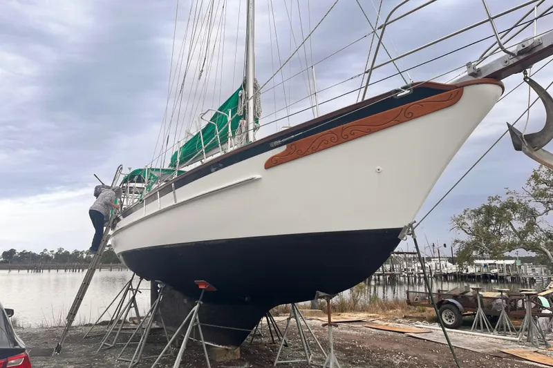 Slide: The Image of 1989 Cabo Rico 34 sailboat on stands, with person climbing ladder, near waterfront. - 8