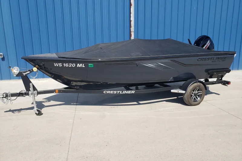 Slide: The Image of 2024 Crestliner 1650 Pro Tiller boat on trailer, covered, parked by blue wall. - 13