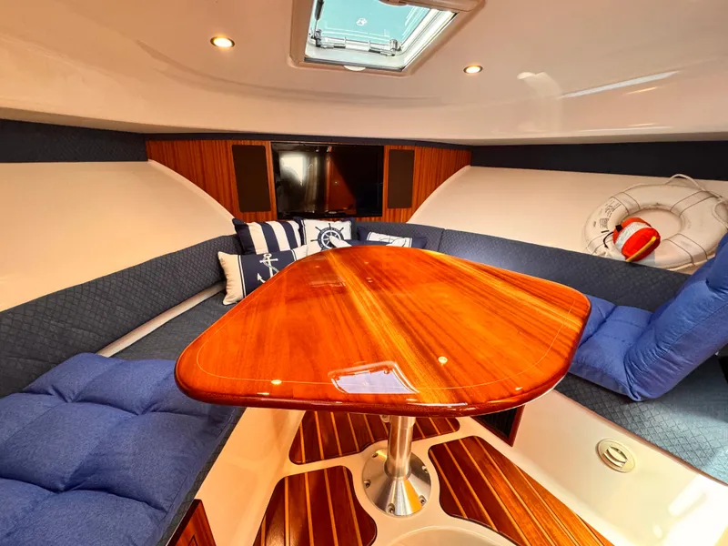 Slide: The Image of 2014 Pursuit OS 385 Offshore cabin with wooden table, blue cushions, and nautical decor. - 13