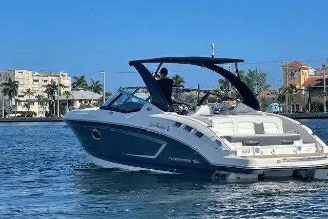 The Image of 2014 Chaparral 307 SSX boat cruising on a sunny waterfront with buildings in the background. - 0