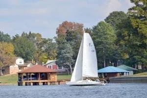 Slide: The Image of Sailboat Corsair F24 MKI 1994 on a serene lake near colorful lakeside houses. - 2