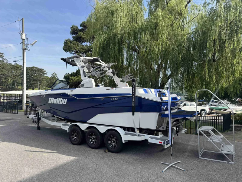 Slide: The Image of 2025 Malibu M242 boat on trailer, parked under trees. - 7