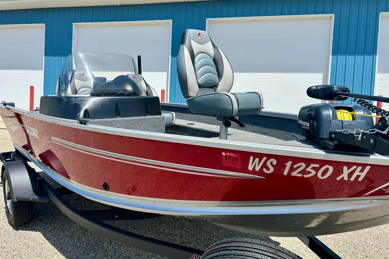 Slide: The Image of 2019 Alumacraft Classic 165 Sport boat in red, parked near blue building. - 4