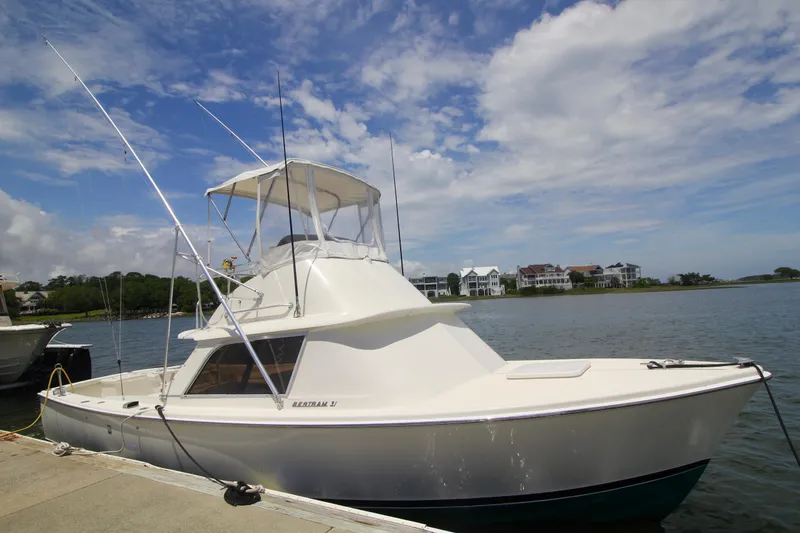 Slide: The Image of 1970 Bertram 31 Sportfisher boat docked by waterfront homes under a partly cloudy sky. - 3