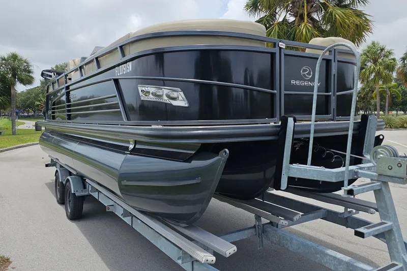 Slide: The Image of 2020 Regency 230 LE3 pontoon boat on trailer, parked near palm trees. - 12