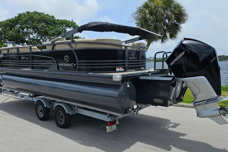 Slide: The Image of 2020 Regency 230 LE3 pontoon boat with Mercury engine on trailer by waterfront. - 2