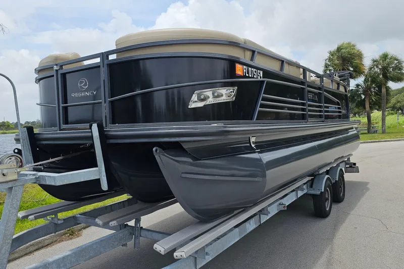 Slide: The Image of 2020 Regency 230 LE3 pontoon boat on trailer, parked near a lake. - 3
