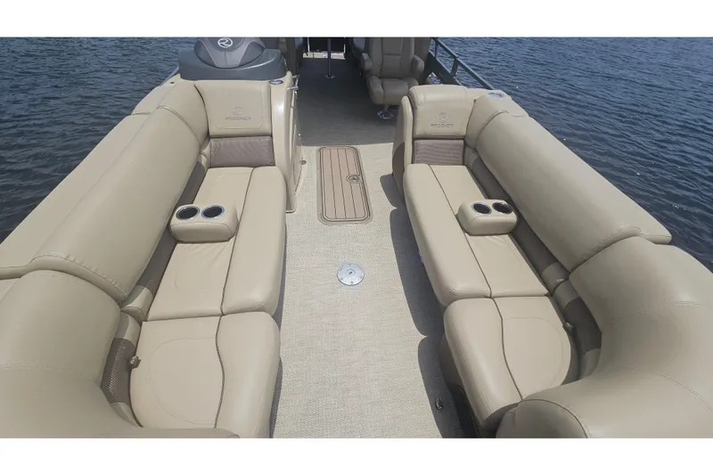 Slide: The Image of 2020 Regency 230 LE3 pontoon boat interior with beige seating and cup holders on the water. - 37