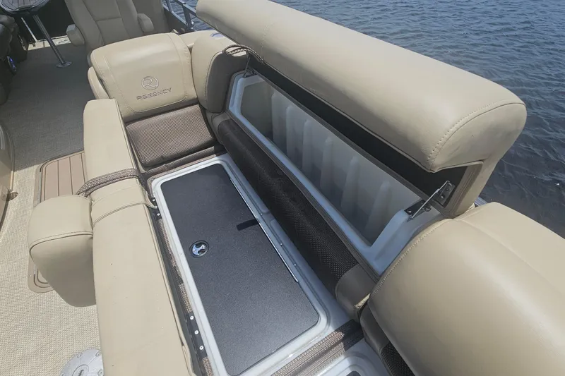 Slide: The Image of 2020 Regency 230 LE3 boat interior with open storage compartment, beige seating, and water view. - 40