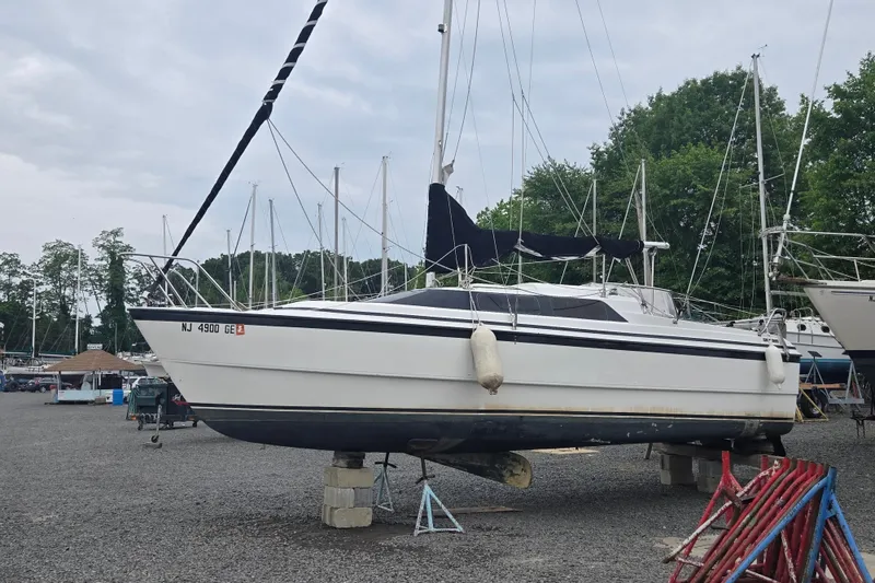 The Image of 1997 MacGregor 26X sailboat on dry dock, surrounded by other boats and trees. - 0