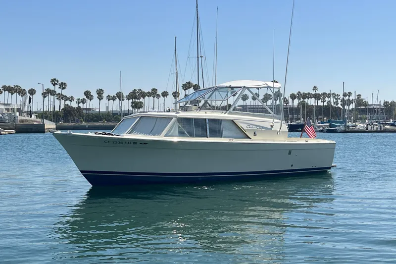 The Image of 1966 Chris-Craft 27 Commander boat on calm water, with marina and palm trees in background. - 0
