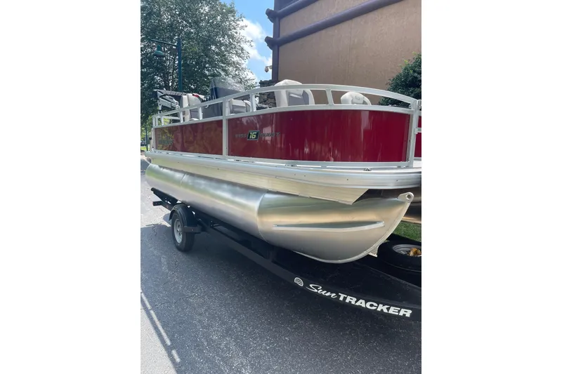 The Image of 2026 Sun Tracker Bass Buggy 16 XL Select pontoon boat on trailer, parked outdoors. - 0