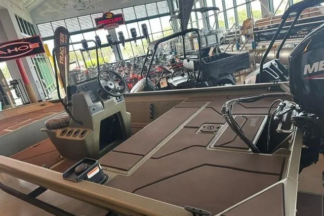 Slide: The Image of 2026 Tracker Grizzly 1860 CC boat interior in showroom, featuring steering console and Mercury engine. - 12