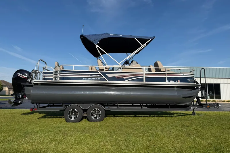 The Image of 2021 Ranger Reata 223F pontoon boat on trailer, blue canopy, parked on grass. - 0