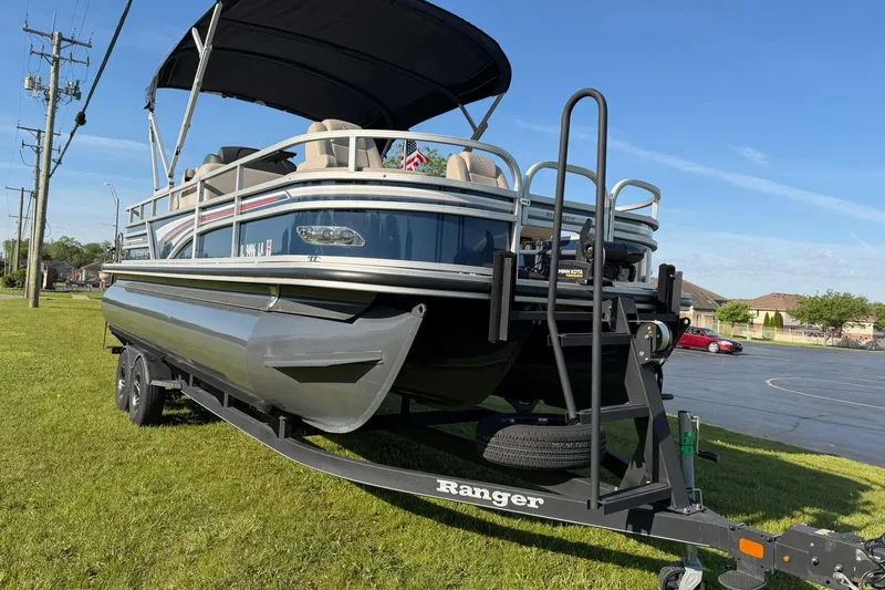 Slide: The Image of 2021 Ranger Reata 223F pontoon boat on trailer, parked on grass under clear sky. - 5