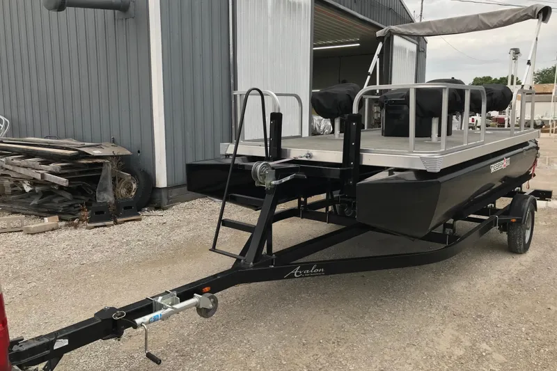 Slide: The Image of 2024 Tigershark 700 12' Mini Pontoon on trailer, parked outside industrial building. - 13