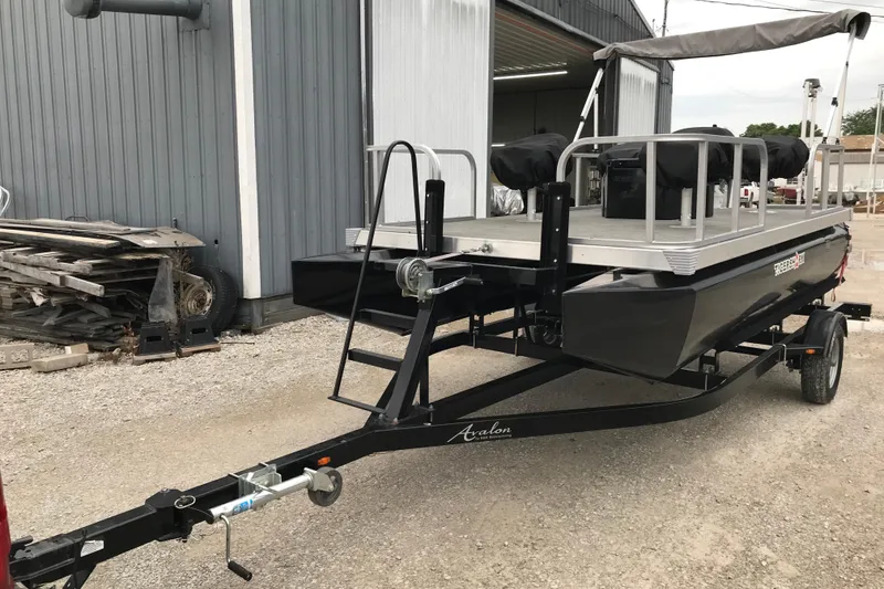 Slide: The Image of 2024 Tigershark 700 12' Mini Pontoon on trailer, parked outside a metal building. - 15
