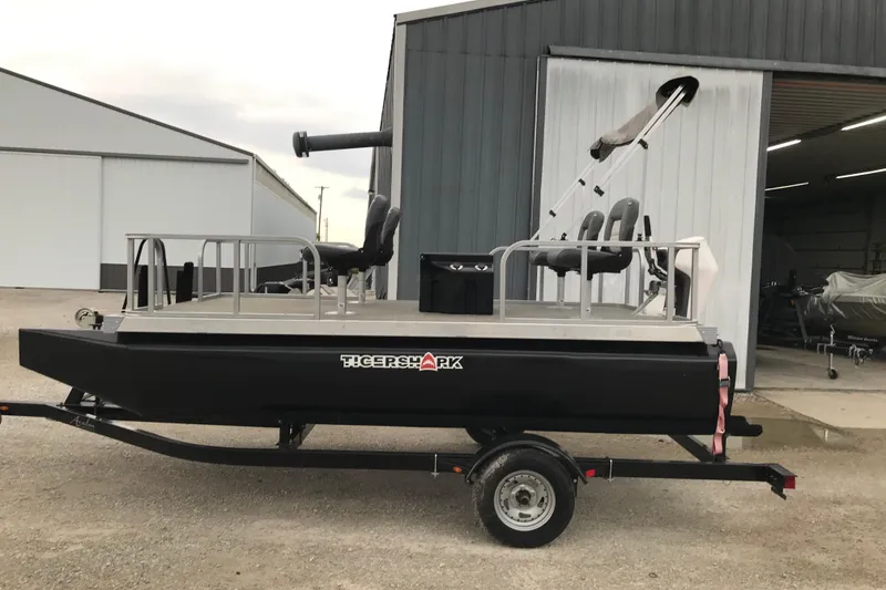 The Image of 2024 Tigershark 700 12' Mini Pontoon boat on trailer outside a warehouse. - 2