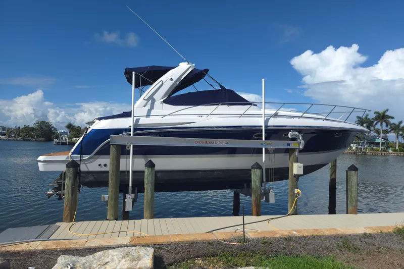 The Image of 2005 Formula 37 Performance Cruiser on lift by waterfront dock, under clear blue sky. - 0