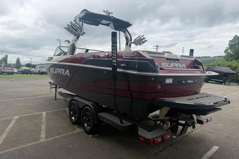 Slide: The Image of 2024 Supra SE 550 boat on trailer in parking lot, showcasing sleek design and maroon color. - 2