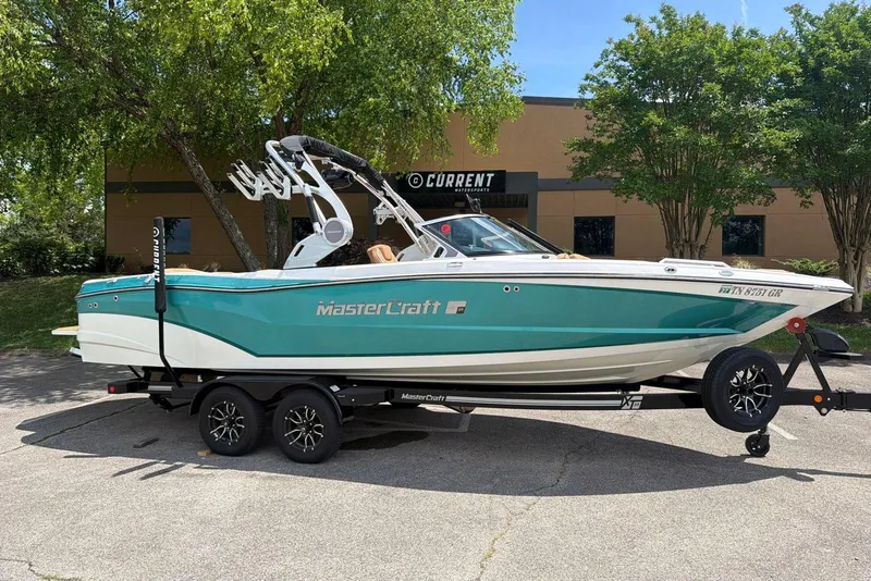 The Image of 2020 MasterCraft XT25 boat on trailer, parked outdoors near trees and building. - 0