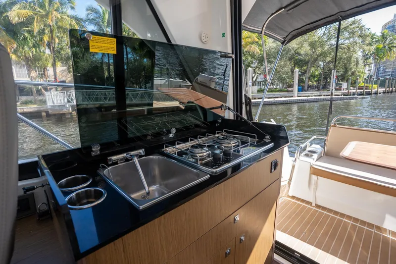 Slide: The Image of 2021 Beneteau Antares 9 boat kitchen with stove, sink, and outdoor seating by the water. - 29