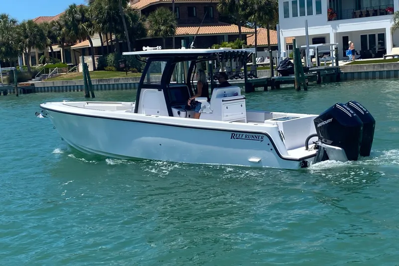 Slide: The Image of 2027 Reef Runner 280 boat cruising on clear blue water near waterfront homes. - 1