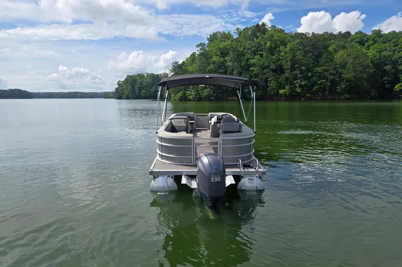 Slide: The Image of 2023 Bennington 22 SSR pontoon boat on a serene lake with lush green surroundings. - 6