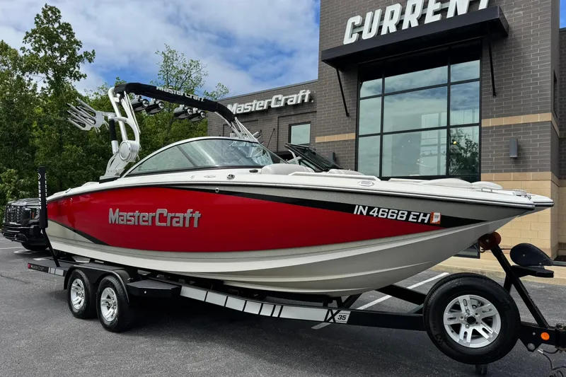 The Image of 2014 MasterCraft X-35 boat in red, parked outside dealership, on a trailer. - 1