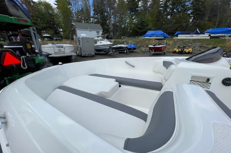 Slide: The Image of 2019 Bayliner Element E16 boat interior with white and gray seating, docked near other boats. - 23