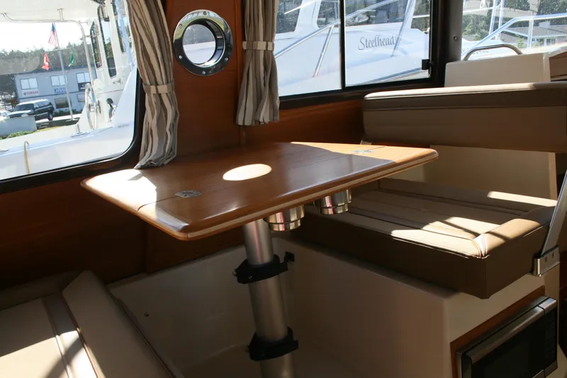 Slide: The Image of 2024 Ranger Tugs R-25 interior dining area with wooden table and cushioned seating. - 11