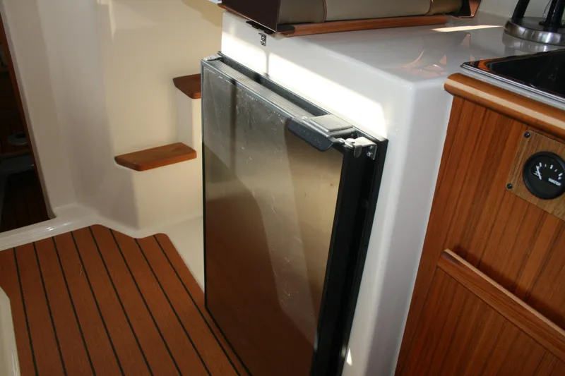 Slide: The Image of 2024 Ranger Tugs R-25 interior with compact refrigerator and wooden cabinetry. - 14