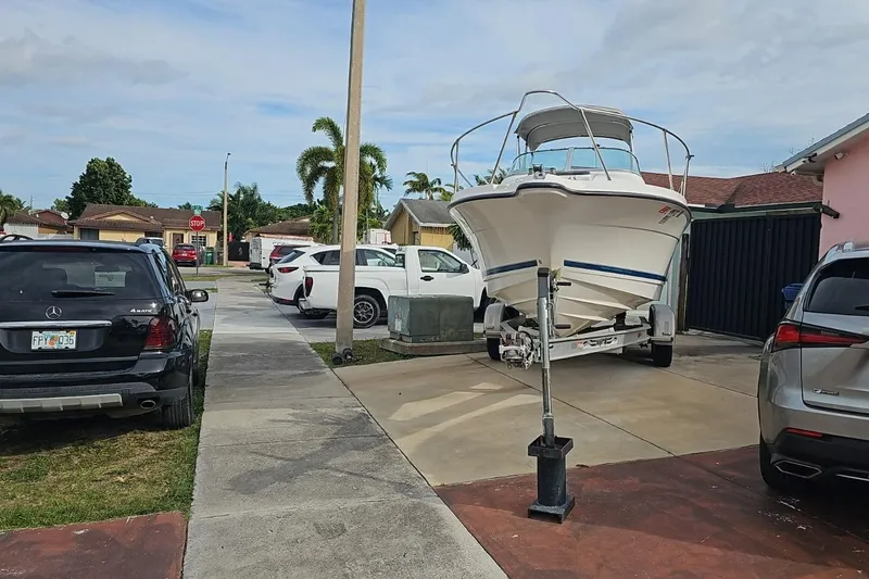 Slide: The Image of 1999 Bayliner 1802 Trophy boat on trailer in suburban driveway, surrounded by parked cars. - 6