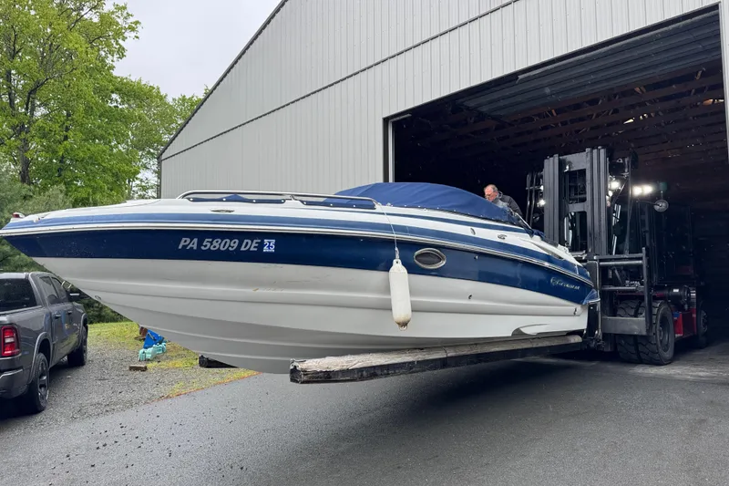 The Image of 2009 Crownline 240 LS boat being moved by a forklift from a storage building. - 2