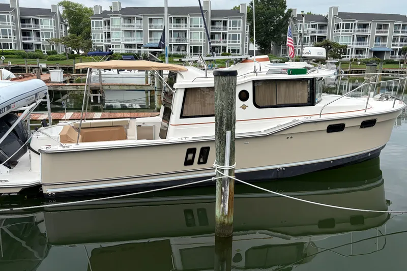 The Image of 2021 Ranger Tugs R-27 boat docked in a marina with waterfront buildings. - 0