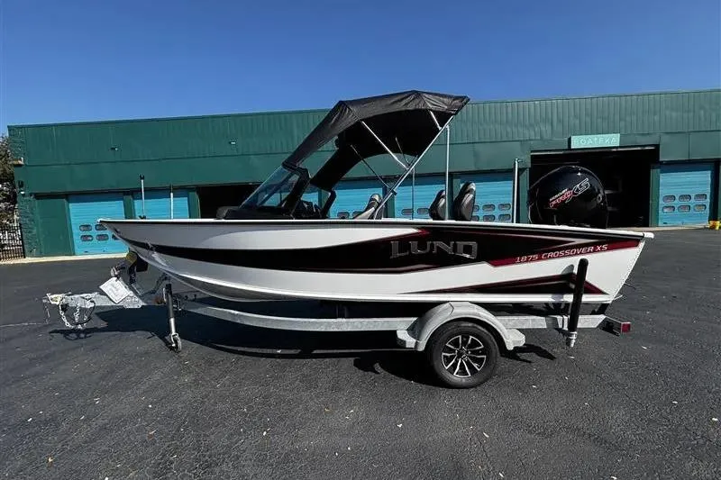 The Image of 2026 Lund 1875 Crossover XS boat on trailer, parked outside a building. - 1