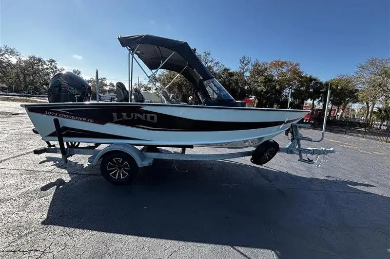 Slide: The Image of 2026 Lund 1875 Crossover XS boat on trailer, parked outdoors under clear sky. - 2