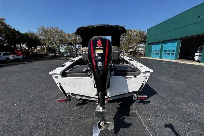 Slide: The Image of 2026 Lund 1875 Crossover XS boat, rear view with outboard motor, parked outdoors. - 3