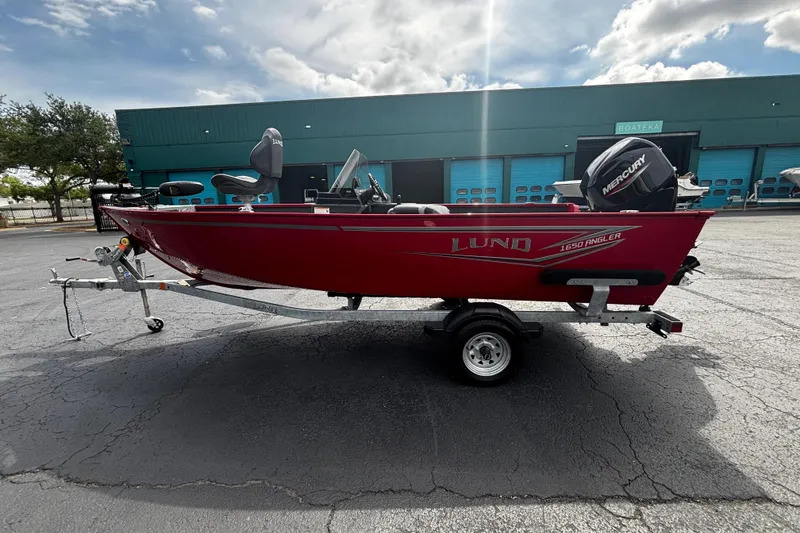 Slide: The Image of 2026 Lund 1650 Angler SS boat on trailer, red exterior, parked outdoors. - 2