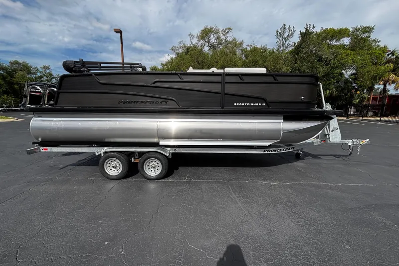 Slide: The Image of 2026 Princecraft Sportfisher 21-2S pontoon boat on trailer, parked outdoors. - 2