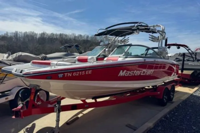 Slide: The Image of 2013 MasterCraft X-45 boat in red and white, parked on a trailer, sunny day. - 1