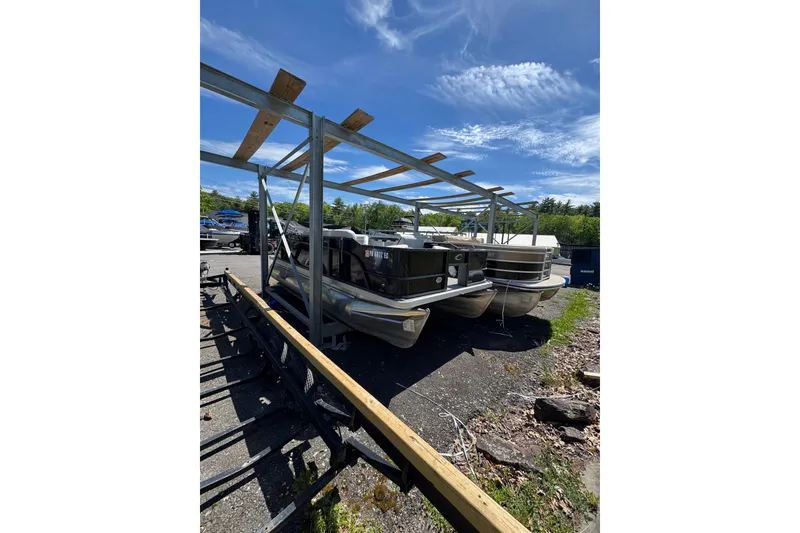Slide: The Image of 2023 Crest CLASSIC LX FISH 200 C4 pontoon boats stored outdoors under a metal frame. - 2