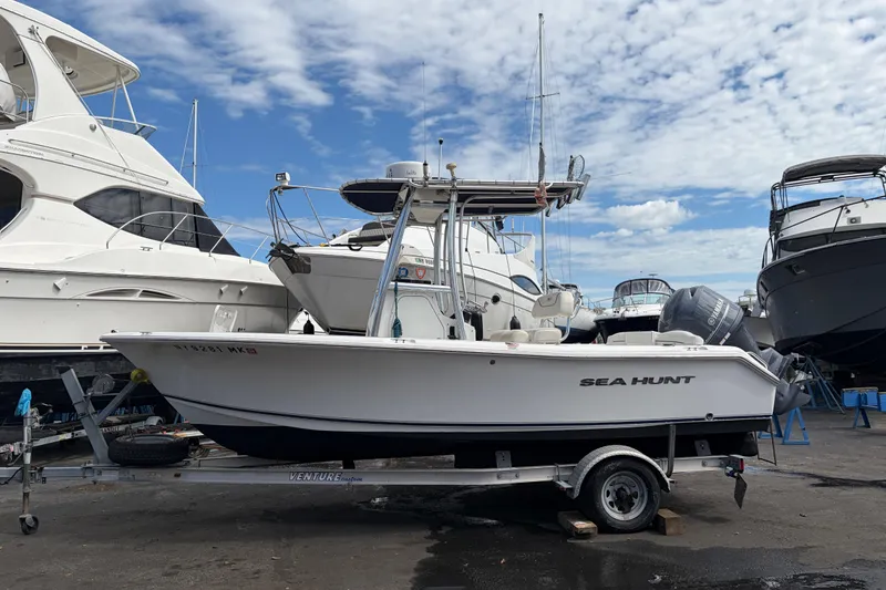 The Image of 2015 Sea Hunt Ultra 196 boat on trailer, surrounded by other boats, under a cloudy sky. - 5