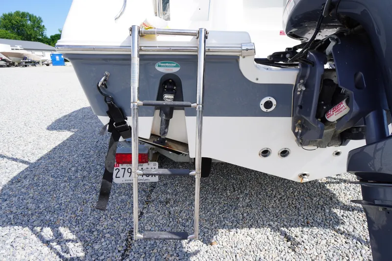 Slide: The Image of 2020 Tidewater 220 LXF boat stern with ladder and motor, parked on gravel. - 37